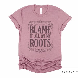 May include: A heather orchid t-shirt with a vintage-style graphic that says "Blame it all on my roots".