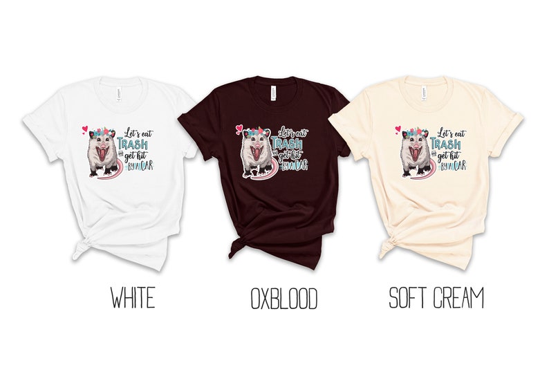 May include: Three t-shirts in white, oxblood, and soft cream. Each shirt features a graphic of an opossum wearing a floral crown, with the text "Let's eat trash & get hit by a car."