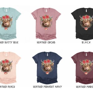 K&ouml;nnte beinhalten: Eine Auswahl an melierten T-Shirts in verschiedenen Farben, jeweils mit einer detaillierten Illustration einer Highland-Kuh mit Blumenkranz. Verf&uuml;gbare Farben sind Heather Dusty Blue, Orchid, Schwarz, Peach, Midnight Navy und Maroon.