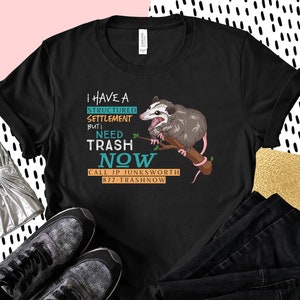 K&ouml;nnte beinhalten: Schwarzes T-Shirt mit einem Grafikdruck eines Opossums, das einen Ast h&auml;lt, mit dem Text "Ich habe eine strukturierte Regelung, aber ich brauche jetzt M&uuml;ll. Rufen Sie JP Junksworth 877-Trashnow an."
