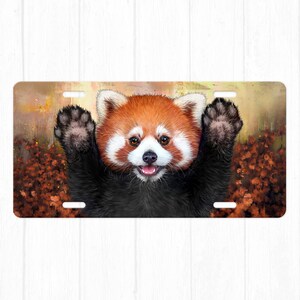 May include: A red panda with black fur and a white chest peeks out from a background of brown and orange leaves. The red panda has a playful expression and is looking directly at the viewer.