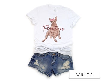 May include: White t-shirt featuring a graphic of a hairless cat wearing a pink bow and the word "Flawless" in maroon lettering.