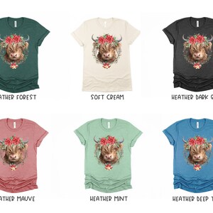 K&ouml;nnte beinhalten: Eine Auswahl an melierten T-Shirts in verschiedenen Farben, jeweils mit einem Highland-Kuh-Motiv. Die Kuh ist mit einem Blumenkranz und einer festlichen Glocke geschm&uuml;ckt. Farben sind unter anderem Waldgr&uuml;n, Creme, Dunkelgrau, Mauve, Mint und Tiefseegr&uuml;n.
