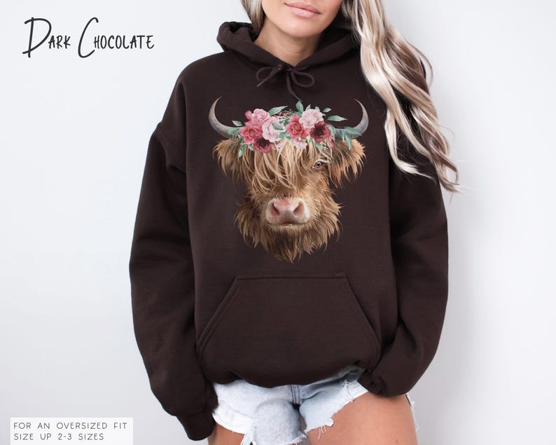 Puede incluir: Una sudadera con capucha de color marr&oacute;n chocolate oscuro con un gr&aacute;fico de vaca de las tierras altas con una corona de flores. El texto "Dark Chocolate" est&aacute; impreso en la parte superior de la sudadera con capucha.