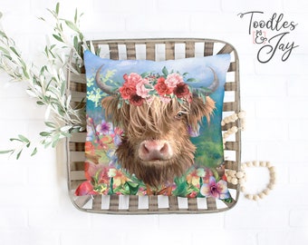 May include: A decorative square pillow featuring a Highland cow with a floral crown. The cow has long, shaggy brown fur and is surrounded by colorful flowers and greenery against a blue background. The pillow is placed in a woven basket.