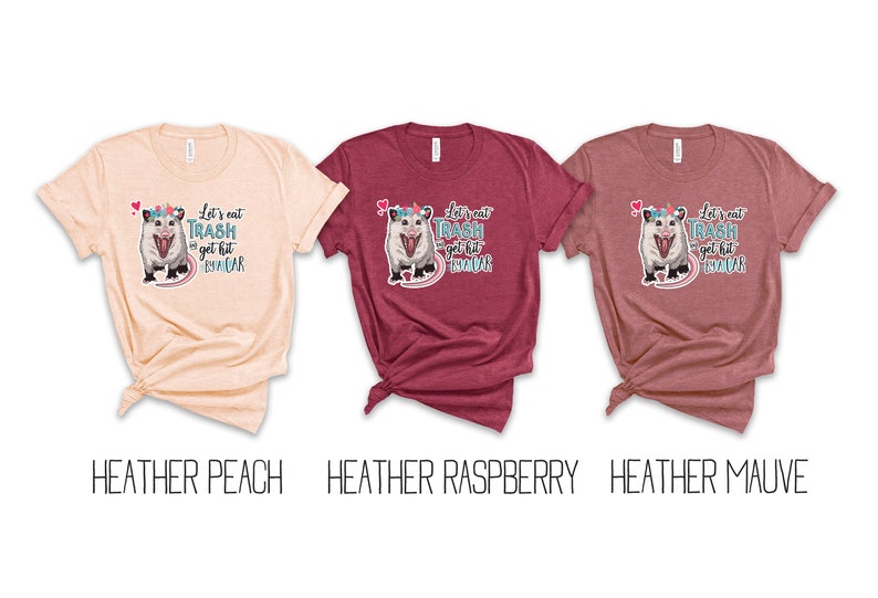 May include: Three t-shirts in heather peach, raspberry, and mauve. Each shirt features a graphic of an opossum with a unicorn horn and the text "Let's eat trash and get hit by a car."