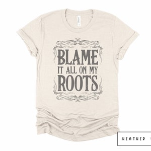 May include: A beige t-shirt with a vintage-style graphic that says "Blame it all on my roots".