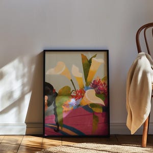 May include: A framed art print featuring a floral still life. The artwork showcases large, cream-colored calla lilies and other colorful flowers in a pink vase. The print is in a black frame and leans against a wall.
