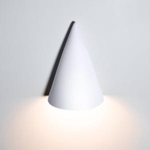 May include: A white cone-shaped wall light fixture with a warm white light emanating from the bottom.