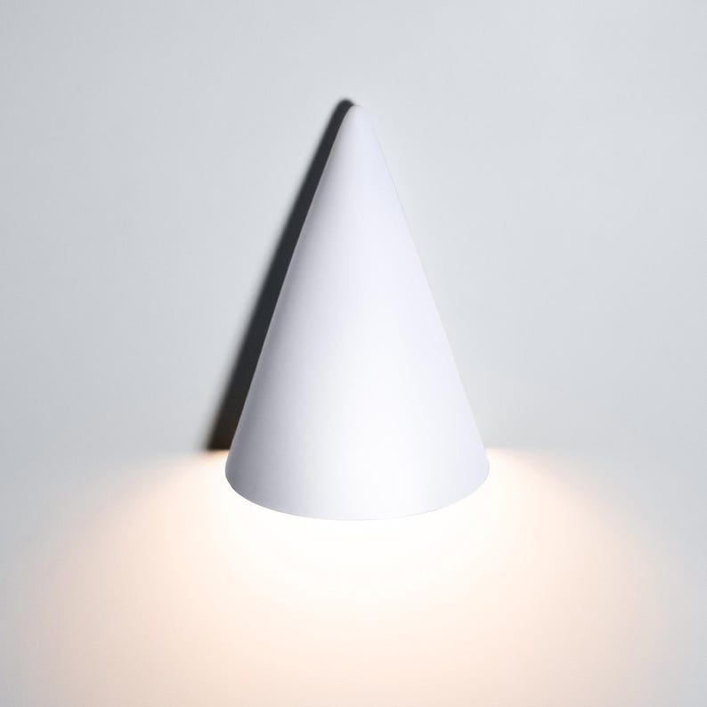 May include: A white cone-shaped wall light fixture with a warm white light emanating from the bottom.