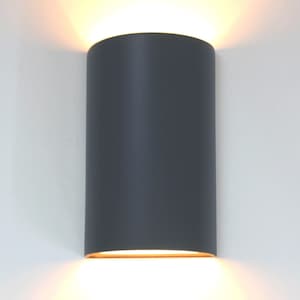 K&ouml;nnte beinhalten: Eine graue zylindrische Wandleuchte mit einem warmwei&szlig;en Licht, das von unten ausstrahlt.