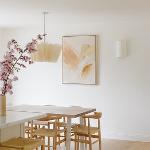 K&ouml;nnte beinhalten: Ein heller Holz-Esstisch mit sechs St&uuml;hlen, einer wei&szlig;en Pendelleuchte und einem hellbraunen abstrakten Gem&auml;lde an der Wand. Eine Vase mit rosa Blumen steht auf dem Tisch.