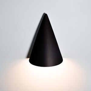 May include: A black cone-shaped wall light fixture with a white light shining from the bottom.
