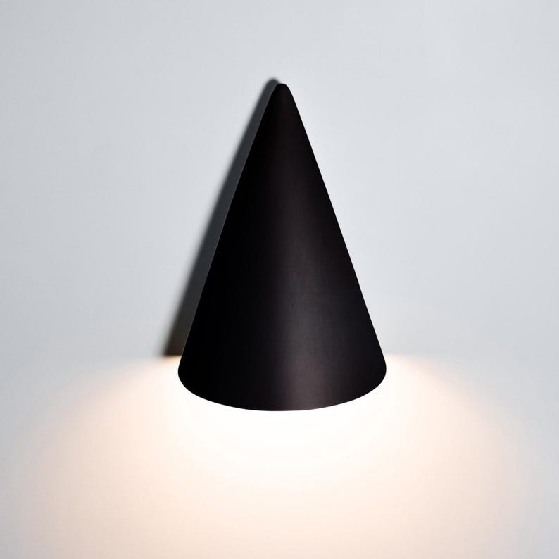 May include: A black cone-shaped wall light fixture with a white light shining from the bottom.