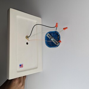 K&ouml;nnte beinhalten: Eine wei&szlig;e Deckenleuchte mit einer blauen Elektrodose und roten Drahtverbindern. Die Leuchte tr&auml;gt ein Etikett mit der Aufschrift "Made in U.S.A."