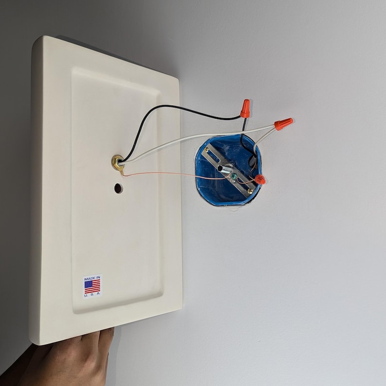 K&ouml;nnte beinhalten: Eine wei&szlig;e Deckenleuchte mit einer blauen Elektrodose und roten Drahtverbindern. Die Leuchte tr&auml;gt ein Etikett mit der Aufschrift "Made in U.S.A."