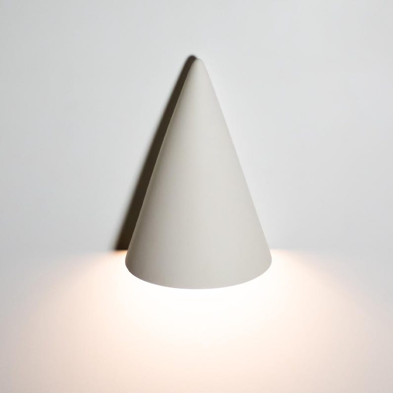 May include: A white cone-shaped wall sconce with a light shining from the bottom.