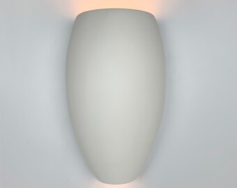 May include: A white, oval-shaped wall sconce with a soft, matte finish. The sconce emits a warm, diffused light from the top and bottom, creating a gentle glow. The fixture is mounted on a white wall, providing a clean and modern aesthetic.