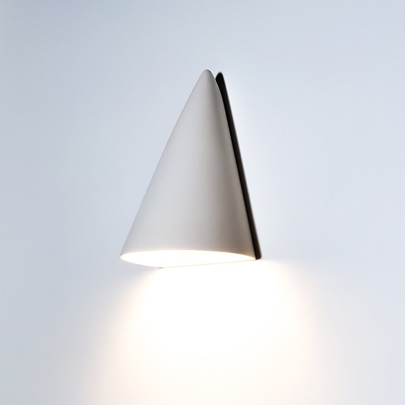 May include: A white cone-shaped wall sconce with a light shining from the bottom.