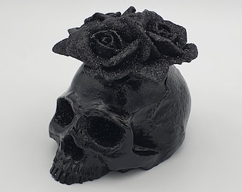 May include: A black skull with a black rose crown on top. The skull is made of resin and has a glossy finish.