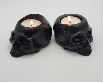 May include: Two black skull-shaped candle holders with tea lights burning inside.