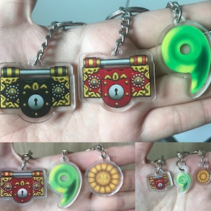 May include: Three sets of keychains featuring a green swirl, a gold and red chest with a keyhole, and a gold coin with a scale design. The keychains are made of clear acrylic and have a silver metal ring.