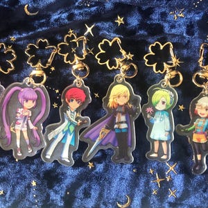 Könnte beinhalten: Acht bunte Anime-Charakter-Schlüsselanhänger mit goldenen Kleeblatt-Anhängern. Die Charaktere sind im Cartoon-Stil dargestellt und tragen verschiedene Outfits.