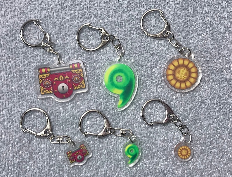 May include: Six keychains with different charms. Two charms are red and gold with a keyhole, one is green and shaped like a number nine, and three are gold with a sun and scales design.