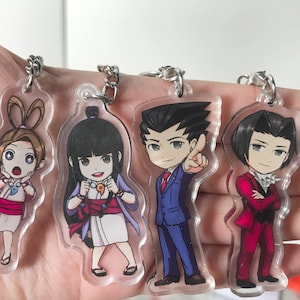 May include: Four clear acrylic keychains featuring anime characters. The characters are a girl with brown hair and a pink bow, a girl with black hair and a blue and white kimono, a man with black hair and a blue suit, and a man with black hair and a red suit.