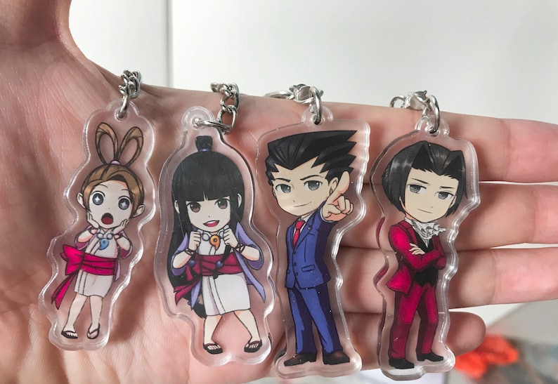 May include: Four clear acrylic keychains featuring anime characters. The characters are a girl with brown hair and a pink bow, a girl with black hair and a blue and white kimono, a man with black hair and a blue suit, and a man with black hair and a red suit.
