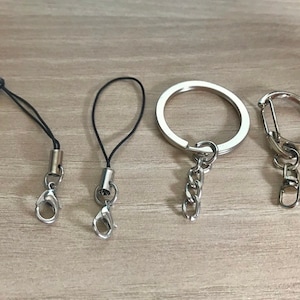 May include: Four keychains with different styles. Two are black string keychains with silver clasps. One is a silver ring keychain with a silver chain. The last is a silver carabiner keychain with a silver chain.