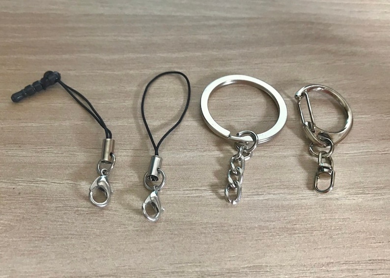 May include: Four keychains with different styles. Two are black string keychains with silver clasps. One is a silver ring keychain with a silver chain. The last is a silver carabiner keychain with a silver chain.