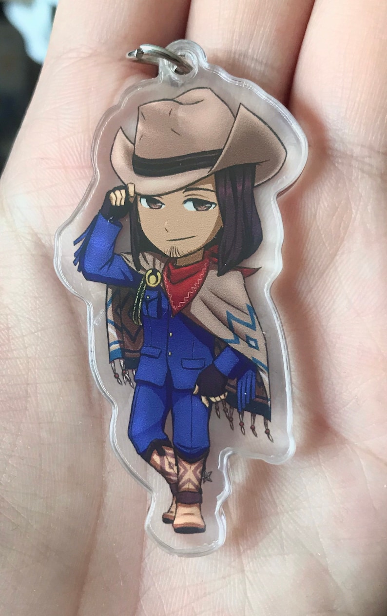 May include: A cartoon character keychain with a cowboy hat, blue jacket, and red bandana. The character is wearing brown boots and a tan poncho with blue and white patterns.