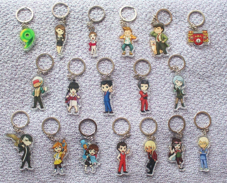 May include: A collection of 18 colorful anime character keychains. The keychains are made of clear acrylic and feature characters from the Ace Attorney series. The keychains are attached to silver key rings.