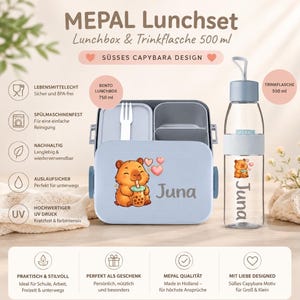 Op de afbeelding: Een Mepal lunchset bestaande uit een 750 ml bento lunchbox en een 500 ml drinkfles. Beide items zijn lichtblauw en voorzien van een cartoon capybara die bubble tea drinkt en de naam Juna. Inclusief een witte vork en diverse producticonen.