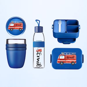 Könnte beinhalten: Ein Set aus blauen Kinder-Lunch-Accessoires, darunter eine Brotdose, eine Wasserflasche und ein runder Behälter. Jeder Artikel zeigt eine rote Feuerwehrwagen-Grafik und den Namen "Emil". Die Brotdose enthält eine Gabel.