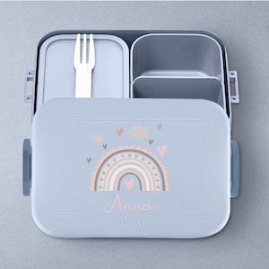 May include: A light blue lunchbox with a rainbow and cloud design. The lunchbox has a removable fork and a compartment for snacks. The lunchbox is personalized with the name "Anna".
