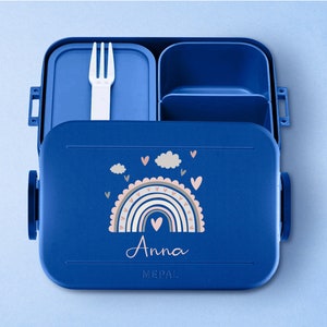 May include: Blue lunchbox with a rainbow and cloud design. The lunchbox has a removable fork and a compartment for snacks. The lunchbox is personalized with the name "Anna".