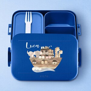 Puede incluir: Fiambrera azul con tapa extra&iacute;ble y un tenedor en el interior. La fiambrera tiene un compartimento para aperitivos y un compartimento m&aacute;s grande para la comida. La fiambrera tiene un dise&ntilde;o personalizado con el nombre "Luca" y una imagen de dibujos animados de animales en un barco.