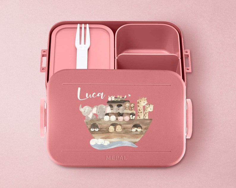 Puede incluir: Lonchera rosa con tapa extra&iacute;ble y un tenedor. La lonchera tiene un compartimento para un s&aacute;ndwich y un compartimento m&aacute;s peque&ntilde;o para refrigerios. La lonchera tiene una ilustraci&oacute;n colorida de un barco con animales. La lonchera tiene el nombre "Luca" escrito en ella.