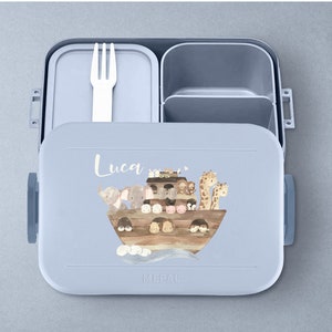 Puede incluir: Una fiambrera azul con tapa extra&iacute;ble y un compartimento separado para cubiertos. La fiambrera tiene una ilustraci&oacute;n colorida de animales en un barco con el nombre "Luca" impreso en la parte delantera.