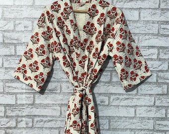 May include: A cream-colored robe with a red floral pattern. The robe is made of a soft fabric and has a tie closure at the waist. The sleeves are three-quarter length, and the robe is hanging on a wooden hanger.