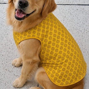 May include: A golden retriever dog wearing a sleeveless yellow shirt with a repeating brown floral pattern. The shirt features a solid yellow trim around the neck and arm openings, providing a snug fit over the dog's back and torso area.