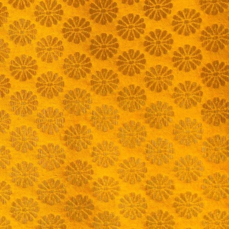 May include: A vibrant golden-yellow fabric featuring a repeating pattern of small, stylised floral motifs. Each flower consists of multiple thin, radiating petals arranged in a circular shape, creating a consistent and dense geometric texture.