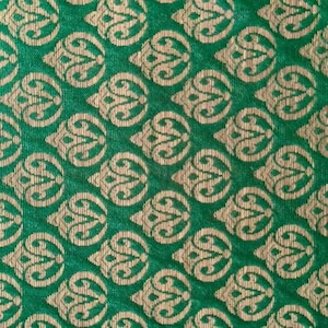 May include: A vibrant green fabric featuring a repeating woven pattern of metallic gold teardrop-shaped motifs. Each motif contains intricate swirling lines and pointed tops, creating a dense, symmetrical design across the entire textile surface.