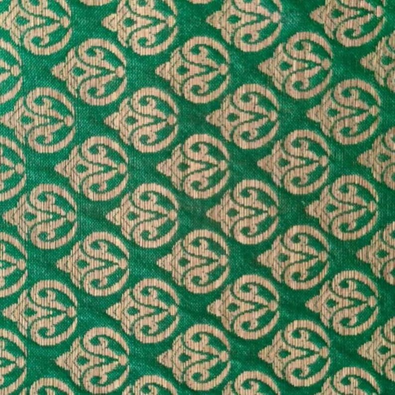 May include: A vibrant green fabric featuring a repeating woven pattern of metallic gold teardrop-shaped motifs. Each motif contains intricate swirling lines and pointed tops, creating a dense, symmetrical design across the entire textile surface.