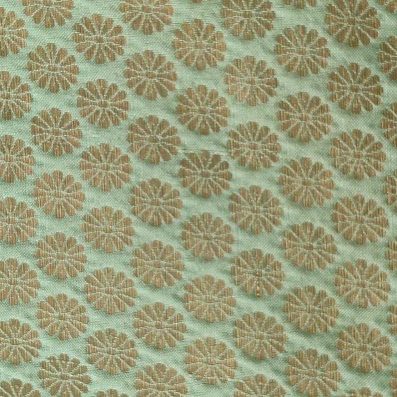 May include: A light mint green fabric featuring a repeating pattern of small, woven golden-brown floral motifs. The textile has a visible, slightly textured weave with a consistent grid of circular flower shapes distributed across the surface.