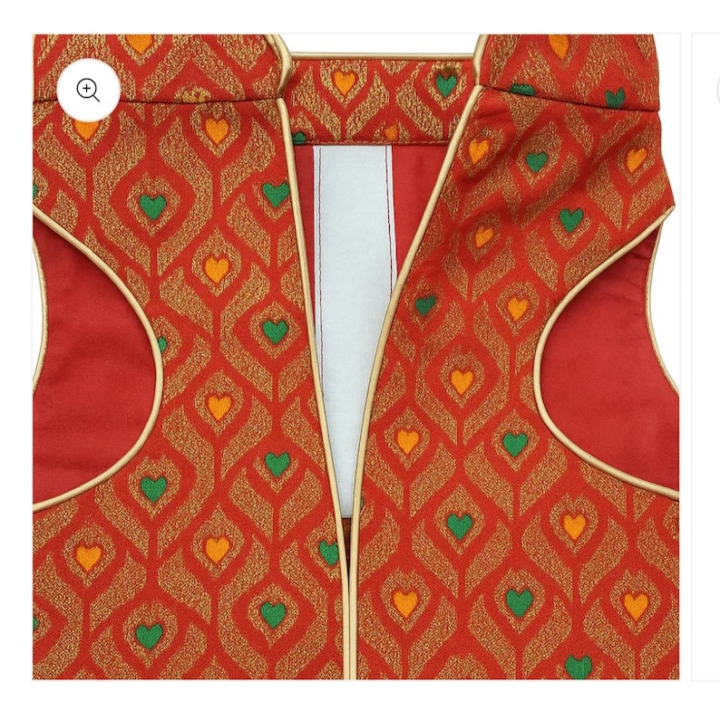 May include: A sleeveless waistcoat in a vibrant red fabric featuring a repeating gold diamond pattern with small green and orange heart-shaped accents. The garment includes gold piping along the armholes and front opening, with a white inner lining.