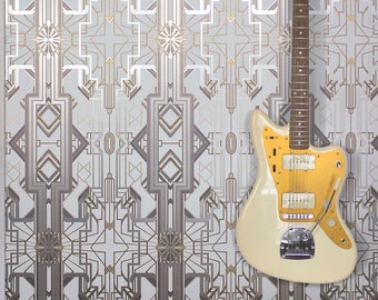 May include: A white electric guitar with a gold pickguard hangs on a wall with a geometric patterned wallpaper. A white piano with black keys and the word "Baldwin" on the front sits below the guitar.