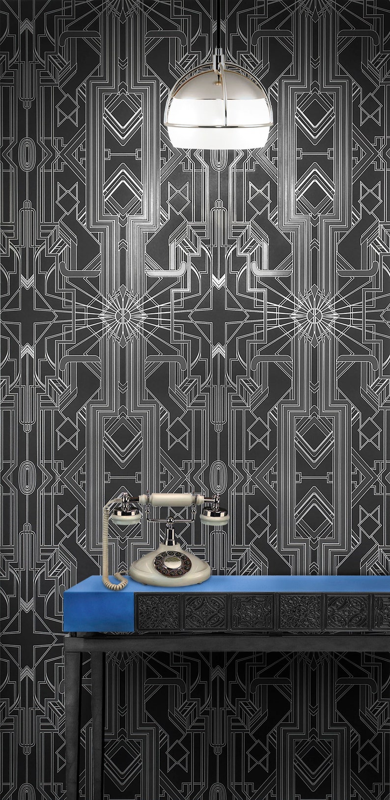 May include: A vintage rotary phone with a white body and black accents sits on a blue table in front of a black and white geometric patterned wallpaper. A chrome and white pendant light hangs above the table.